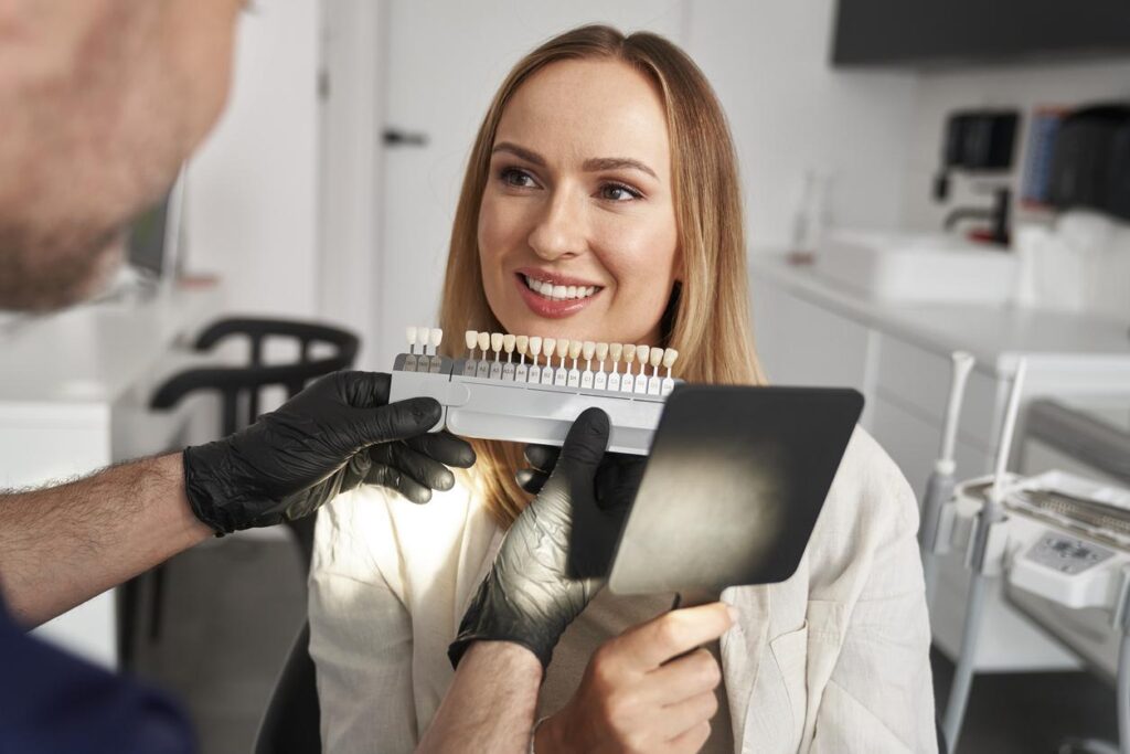 A woman getting a cosmetic dentistry consultation as a dentist holds up dental veneer samples to color match them to her smile
